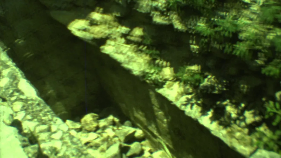 1973 8mm frame from Yucatan looking down into a deep stone-walled shaft or trench beside ruins and vegetation.