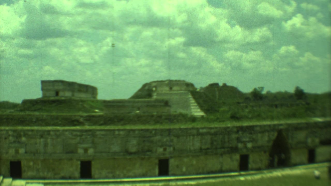 1973 8mm view in Yucatan, Mexico, showing weathered stone ruins, stepped structures, vegetation, and cloudy sky.