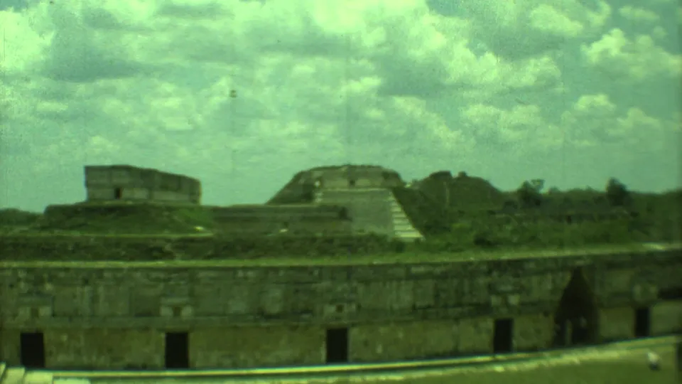 1973 8mm view in Yucatan, Mexico, showing weathered stone ruins, stepped structures, vegetation, and cloudy sky.