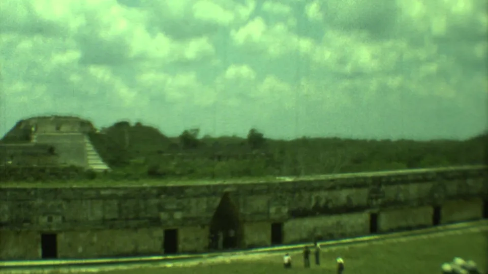 1973 Yucatan, Mexico 8mm frame showing stone ruins, a stepped temple form, cloudy sky, and small visitors on the grounds.