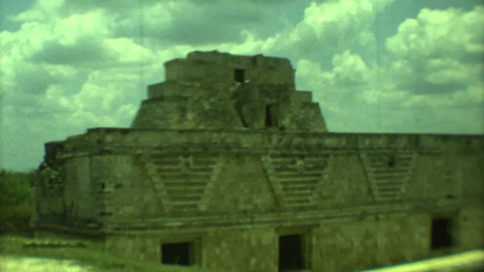 1973 8mm Yucatan travel frame of a weathered stepped ruin, with patterned stonework and vegetation at the edge.