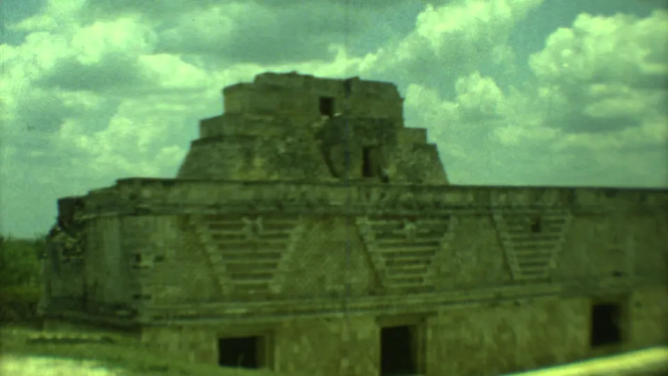 1973 Yucatan 8mm frame of a stepped stone ruin with dark door openings, geometric stonework, and cloudy sky.