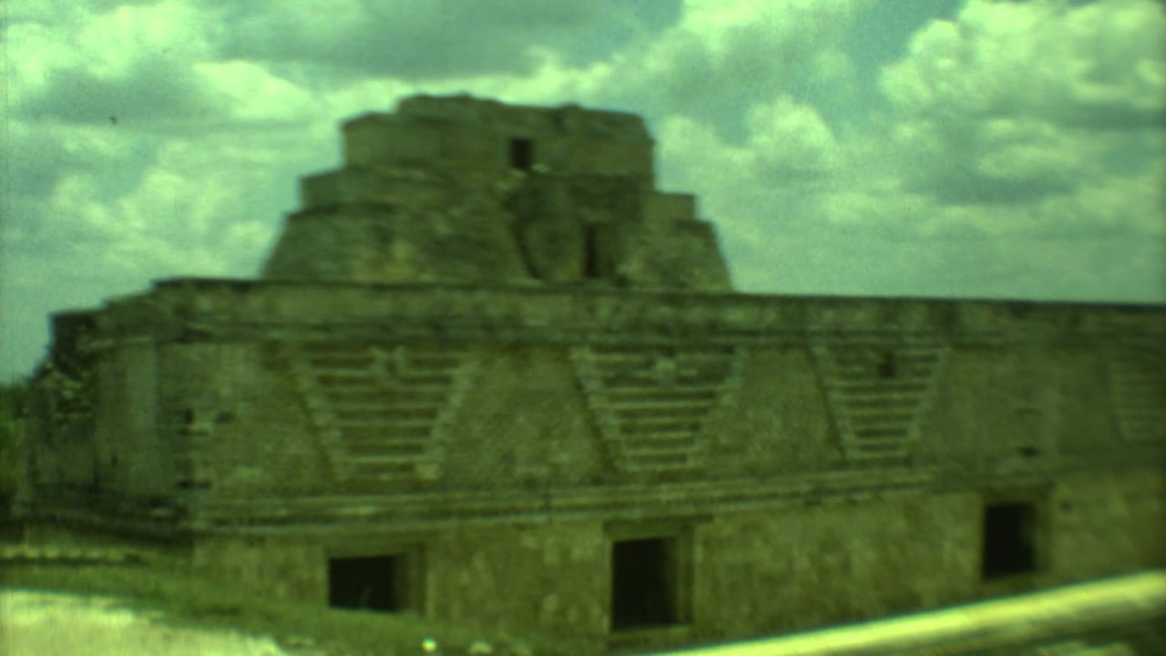 1973 Yucatan 8mm frame showing a large stepped stone ruin, dark doorways, and a cloudy midday sky.