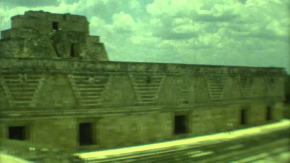 1973 Yucatan home-movie frame of a long stone ruin with stepped forms, stairs, and dark openings.