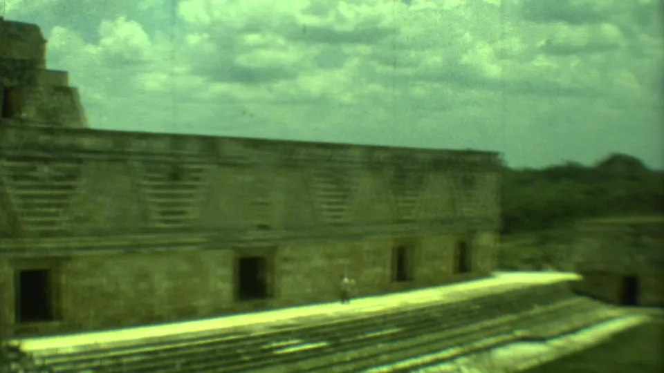 1973 Yucatan 8mm frame showing stone ruins, a bright walkway, and a distant visitor in the courtyard.