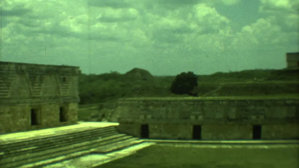 1973 Yucatan ruin footage showing stepped stonework, low masonry walls, distant greenery, and a bright cloudy sky.