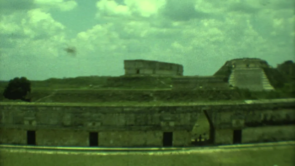 1973 Yucatan 8mm frame with low stone walls, a distant stepped pyramid, and tiny visitors near the right edge.
