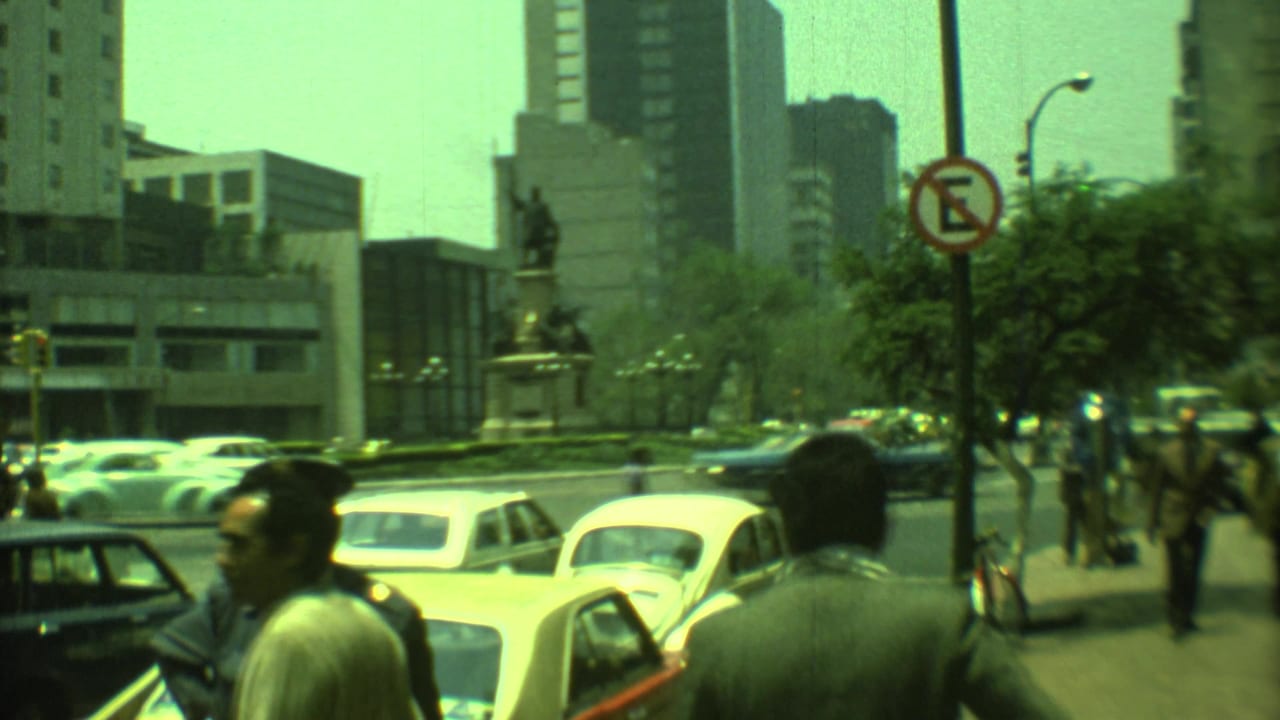 Street-level view of parked and moving cars near a monument plaza and office buildings.
