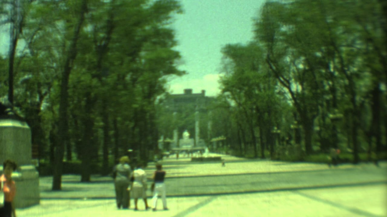 1973 8mm view in Yucatan, Mexico, showing visitors on a broad tree-lined walkway leading toward a distant statue and columns.
