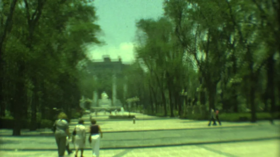 A visitor-shot 1973 Yucatan scene with people crossing a wide paved path toward a formal monument beyond the trees.