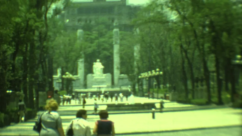 1973 8mm frame from Yucatan, Mexico, looking down a broad promenade toward stone columns, a statue, and scattered pedestrians.