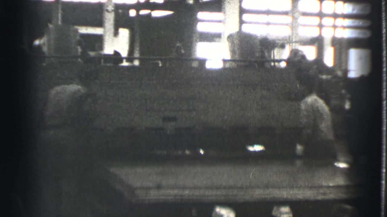 Factory worker beside a large machine in a dim industrial interior.