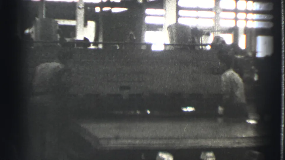 1939 Cleveland factory interior with a worker standing near a large machine under bright windows and overhead lights.