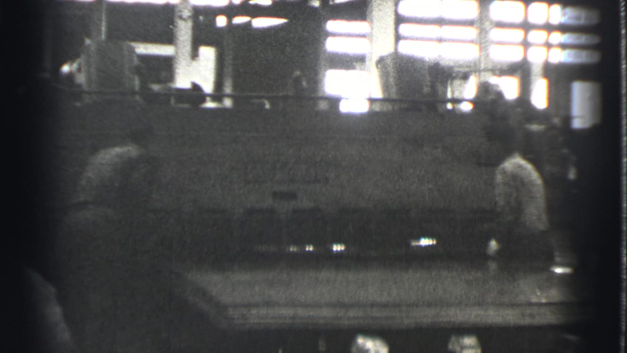 Worker standing near machinery with bright factory windows behind.