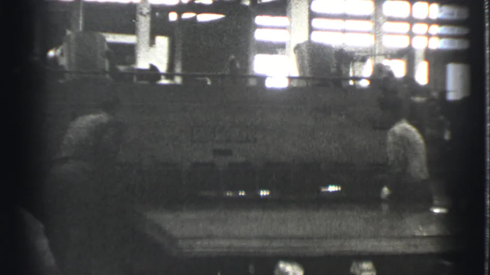 A Cleveland factory worker appears near a large machine, with high windows and interior equipment visible in the background.