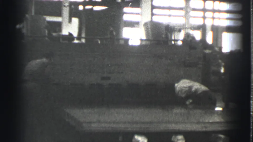 A worker bends at a station beside a large machine in the 1939 Cleveland industrial interior.