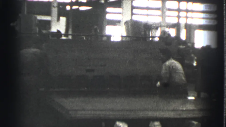A worker crouches or bends beside large industrial equipment inside the Cleveland factory space.