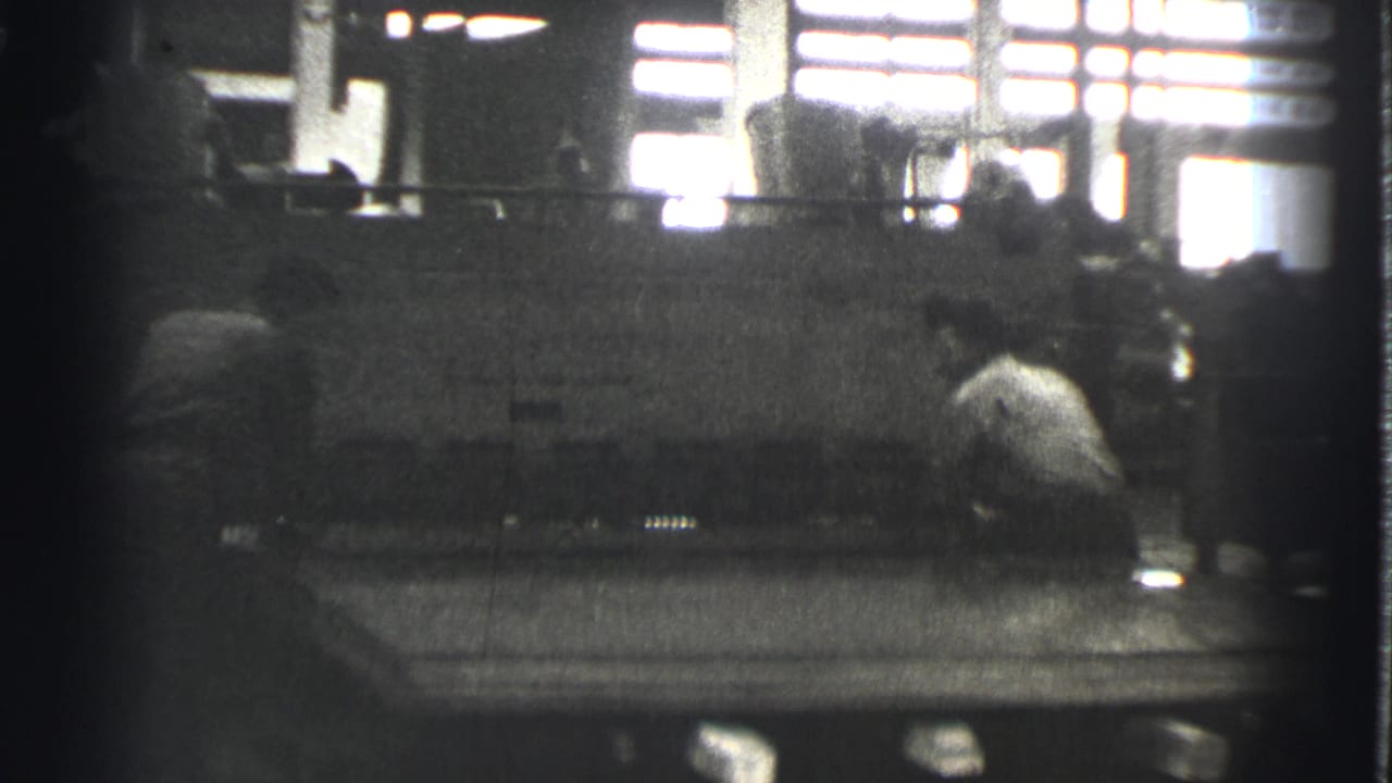 Two workers near a large sheet metal press inside a dim factory.