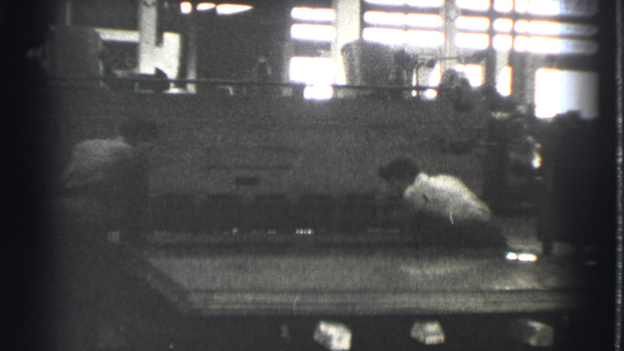 A worker in a light shirt leans near the side of a large press.