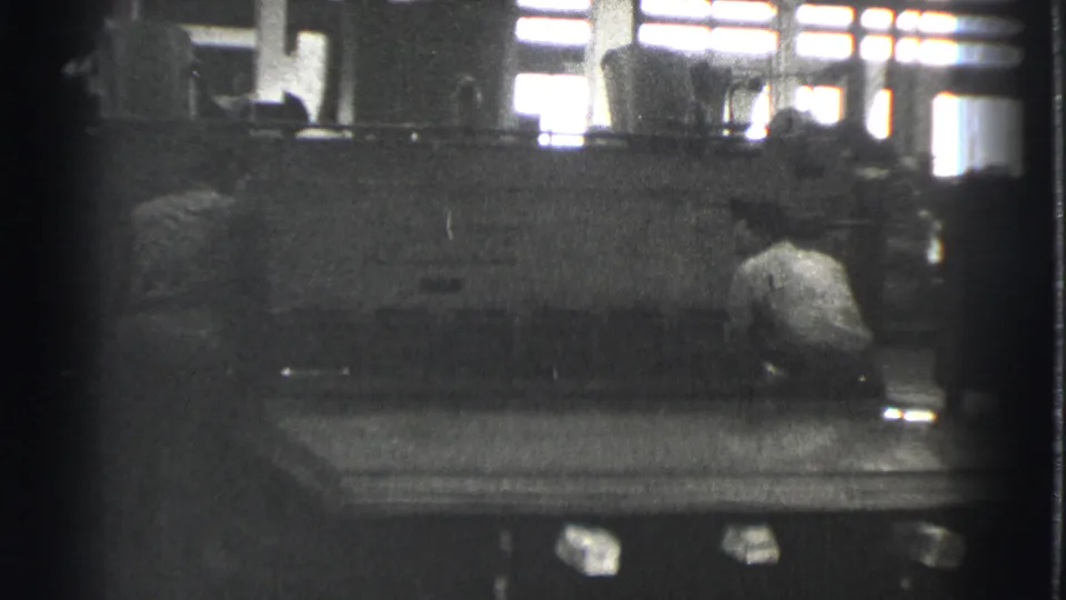 Two adult workers are positioned around a large sheet metal press in the 1939 Cleveland industrial interior.