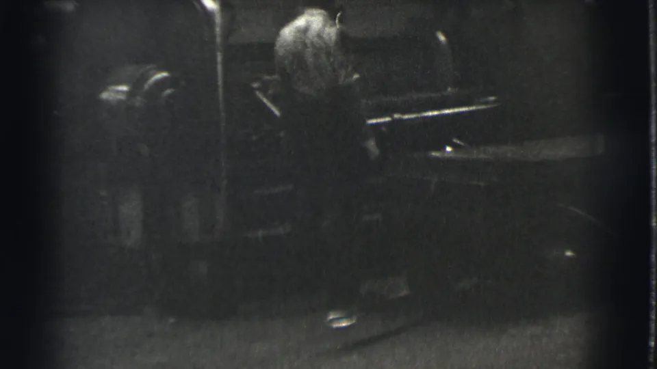 In 1939 Cleveland footage, a man appears beside large industrial machinery in a shadowed black-and-white factory setting.