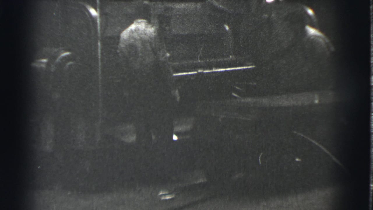 A man in a light shirt stands at a machine while another figure is nearby.