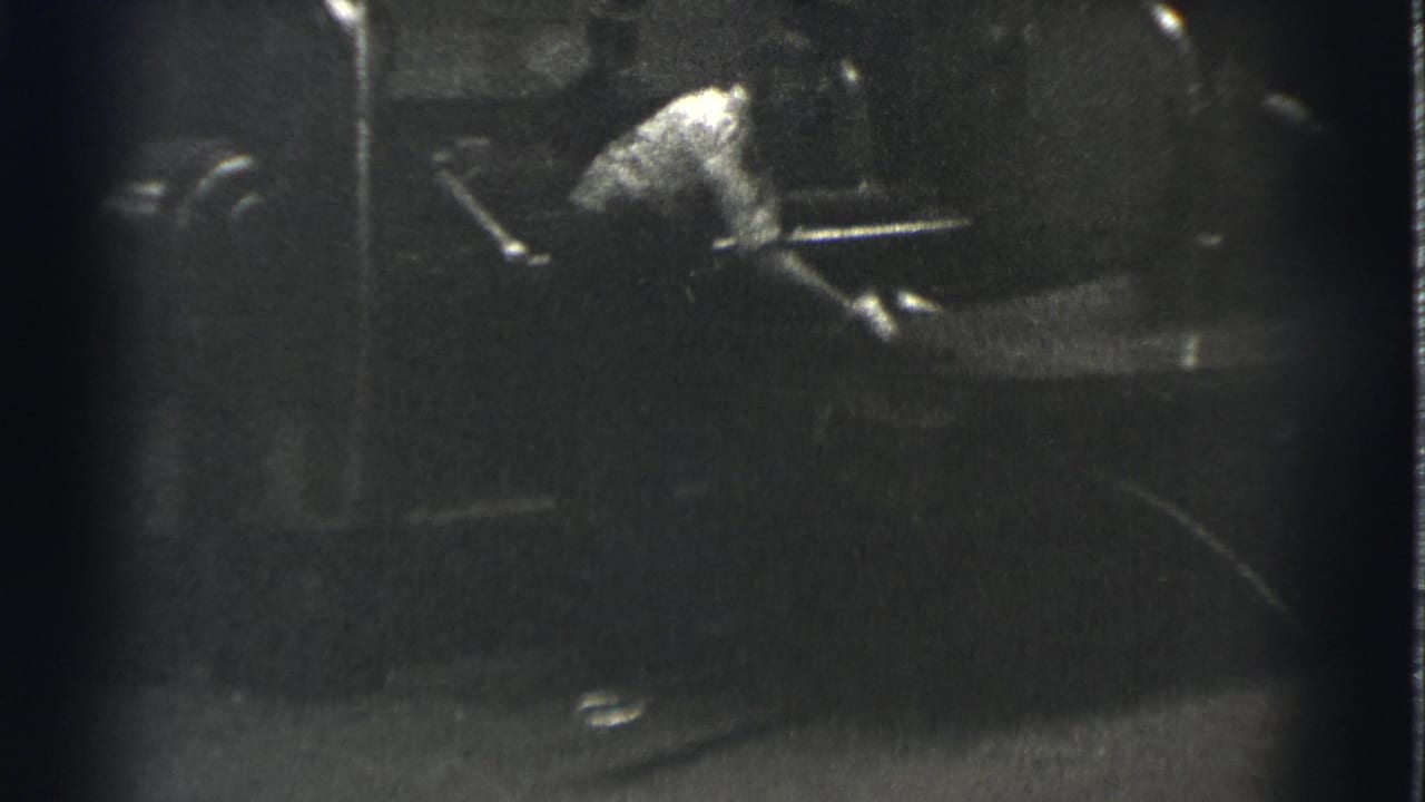 Man in a light shirt bends over machinery in a dark industrial space.