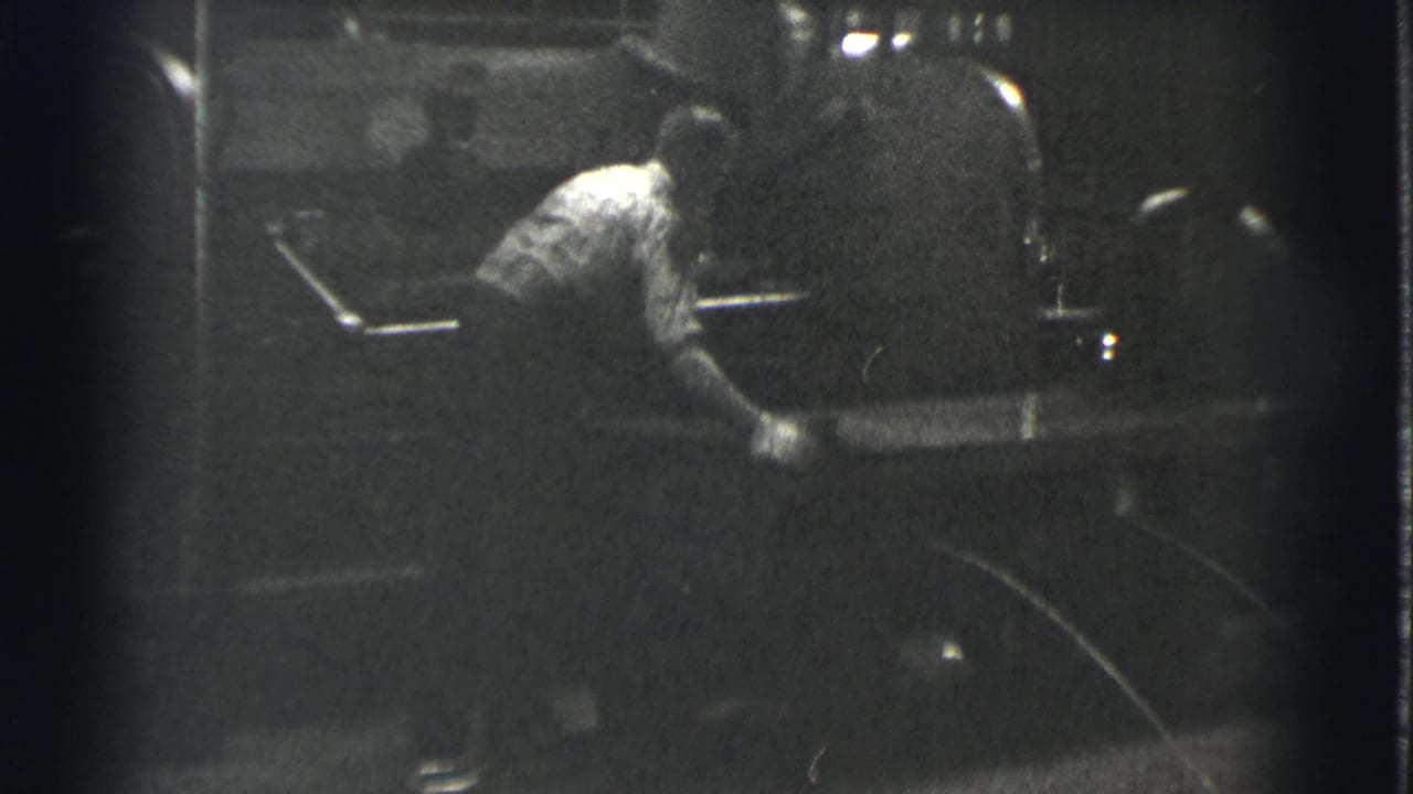 Worker leans forward beside a large rounded machine in low light.