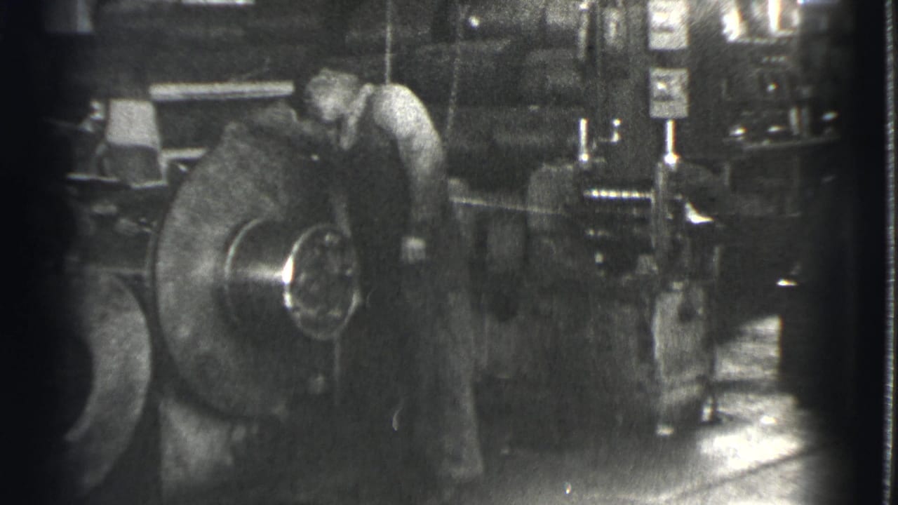 Man in a light shirt works beside a large rotating metal wheel.