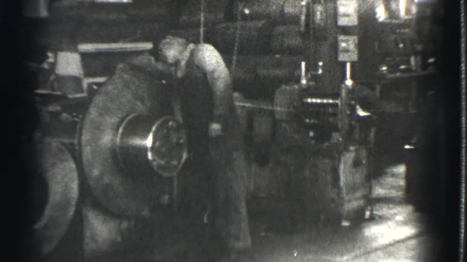 A factory worker appears to monitor or adjust a large rotating machine part in 1939 Cleveland industrial footage.
