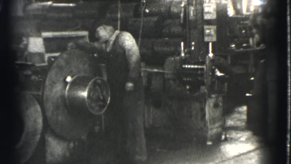 A man works beside a large spinning industrial component in dim 1939 Cleveland factory footage.