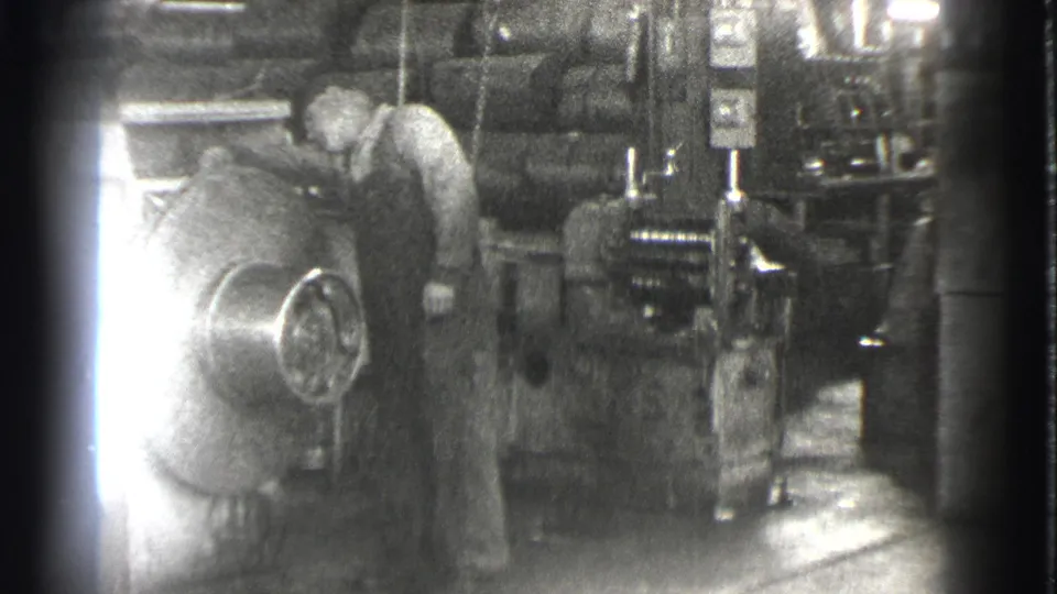 The final frame shows the worker near the large machine, with strong exposure flare and heavy 8mm grain across the factory interior.