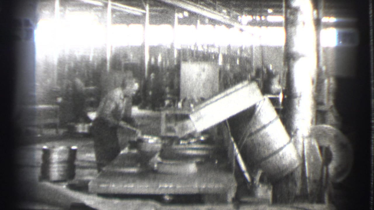Worker operating machinery beside large angled equipment on a factory floor.