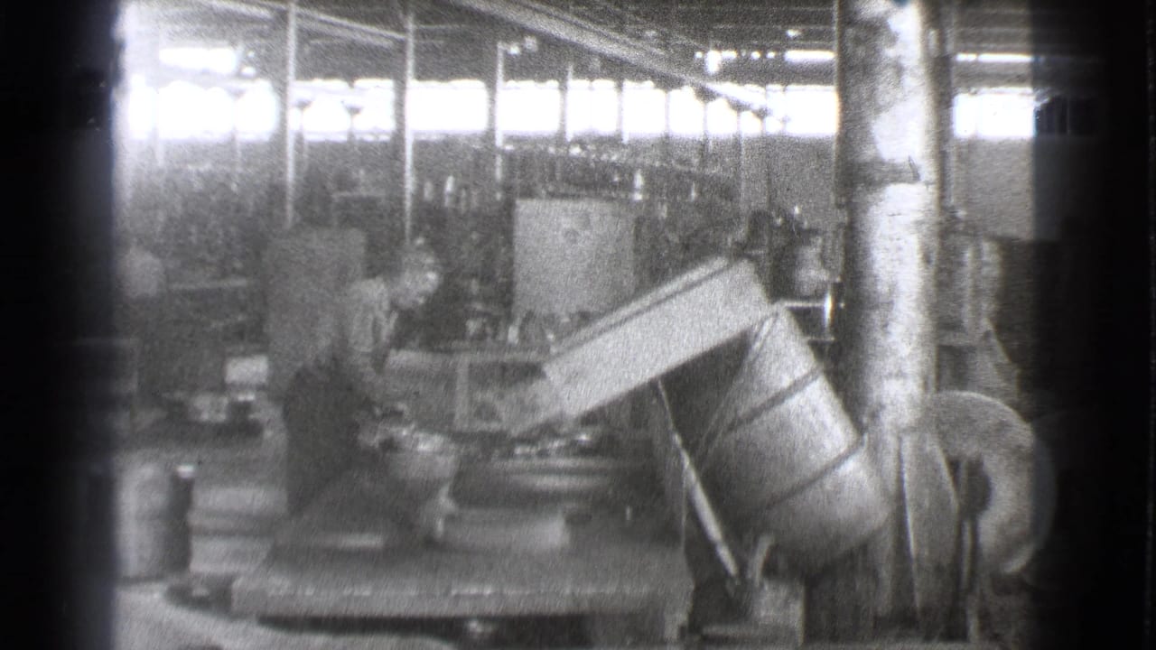 Factory worker leaning near heavy equipment and a large angled machine part.