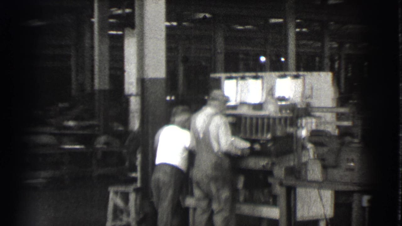 Two workers lean near machinery as the camera pans across the workshop.