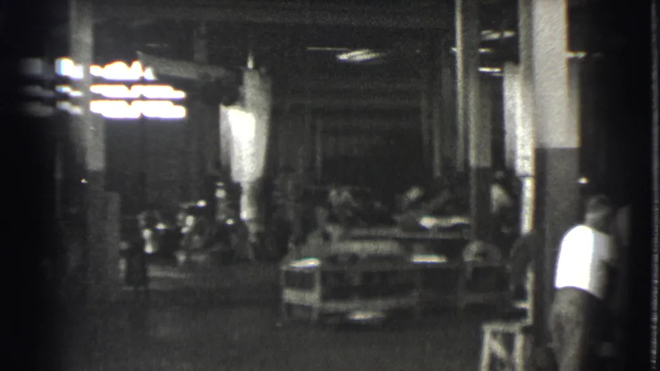 The 1939 Cleveland factory pan opens onto a darker shop floor with machinery, overhead lights, and a worker partly visible at right.
