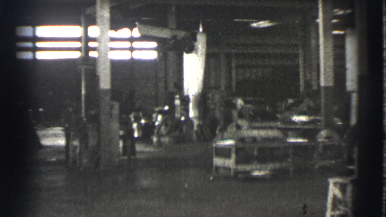 1939 Cleveland industrial interior showing bright high windows, columns, machinery, work tables, and faint workers in shadow.