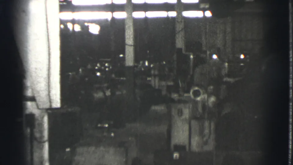 Late-1930s Cleveland industrial space with machinery, columns, bright upper windows, and indistinct workers in the background.