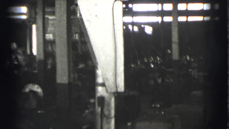 A 1939 factory interior shows machines and columns, with a worker shape near the lower edge and bright windows beyond.