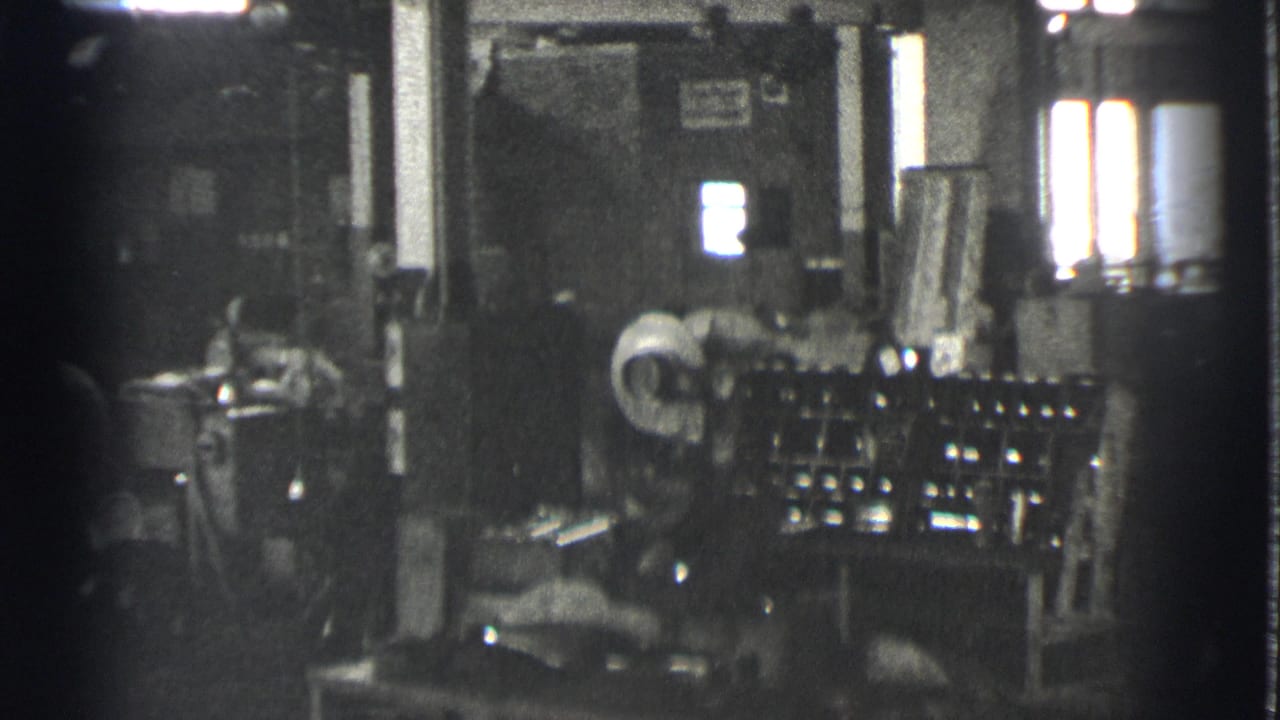 Dim factory interior with a worker near large machinery and bright windows.