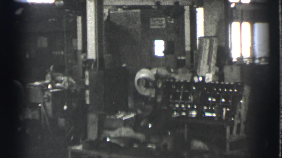 1939 Cleveland factory interior showing a worker beside large industrial equipment in grainy 8mm footage.