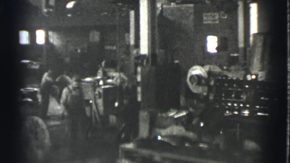 Men in work clothes move through a Cleveland factory interior with large machinery and bright window light.