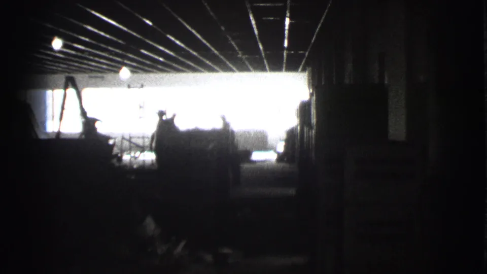 A dark Cleveland factory passage shows silhouetted workers against a bright exit or loading-bay opening.
