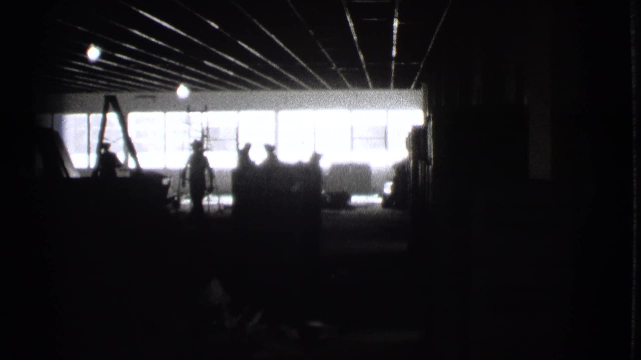 1939 Cleveland 8mm frame showing a very dark industrial-looking interior, bright window wall, ceiling lines, and silhouetted people.