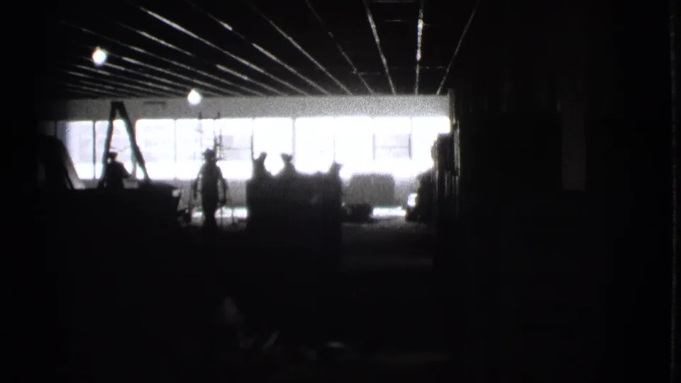 1939 Cleveland 8mm frame showing a very dark industrial-looking interior, bright window wall, ceiling lines, and silhouetted people.