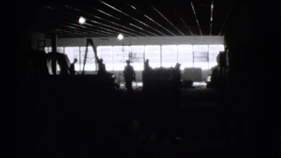 1939 Cleveland home-movie frame with silhouetted figures in a dark factory-like room against large bright windows.