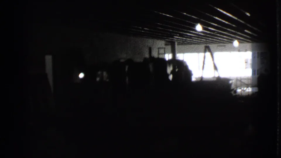 A dim Cleveland interior on 8mm film, with ceiling beams, window glare, and stacked objects visible in silhouette.