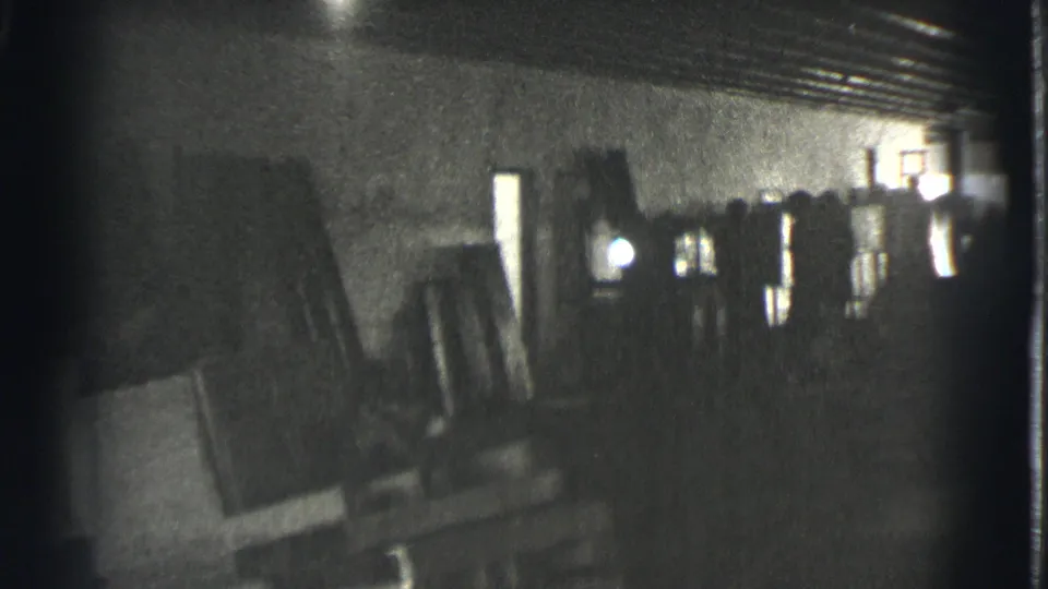 A grainy 1939 Cleveland home-movie frame shows leaning frames, dark wall space, and stored objects in a private interior.