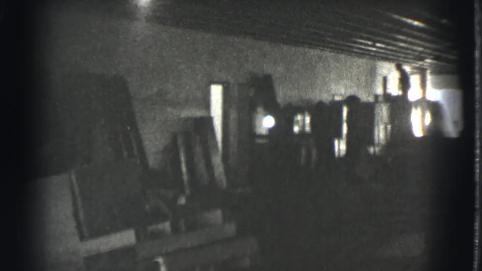 The frame shows a shadowed Cleveland industrial or storage space, with indistinct equipment or crates and a small bright opening.