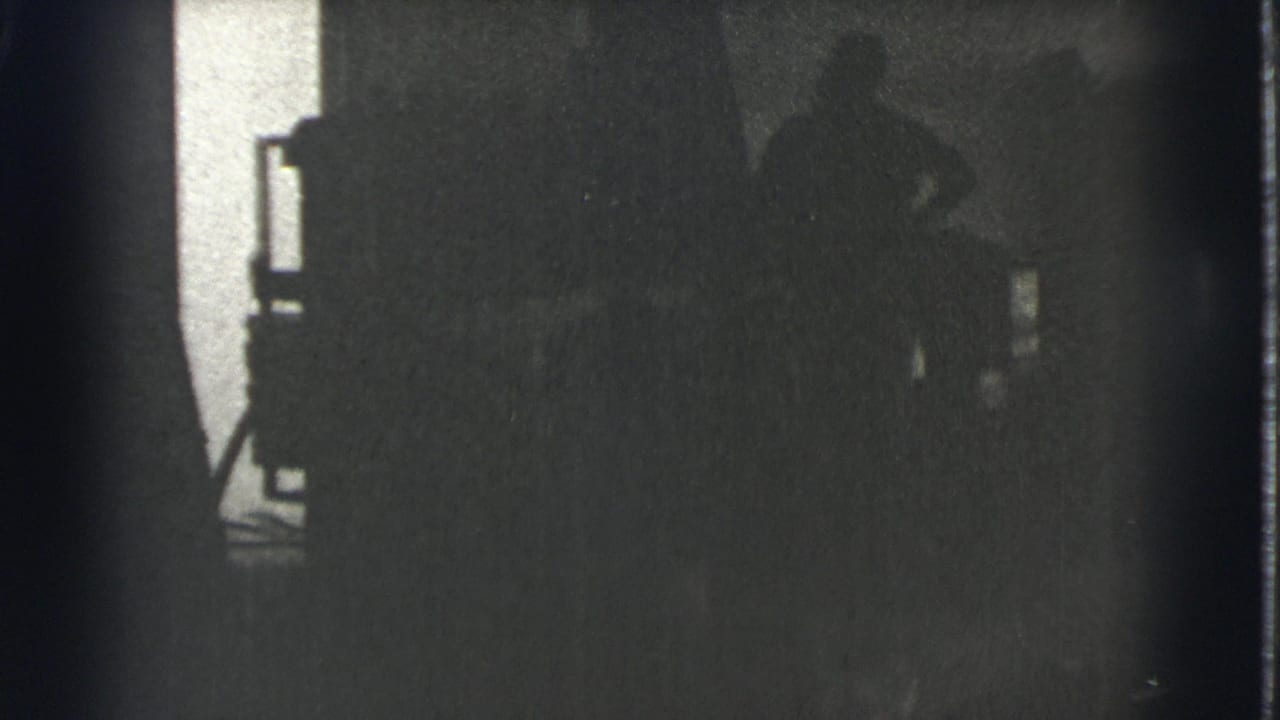 Silhouetted people stand in a dark room beside a bright vertical light source.